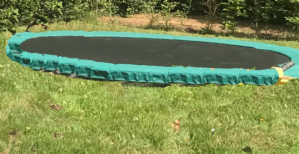 Een ingegraven trampoline in het gras, met een beukenhaag erachter.